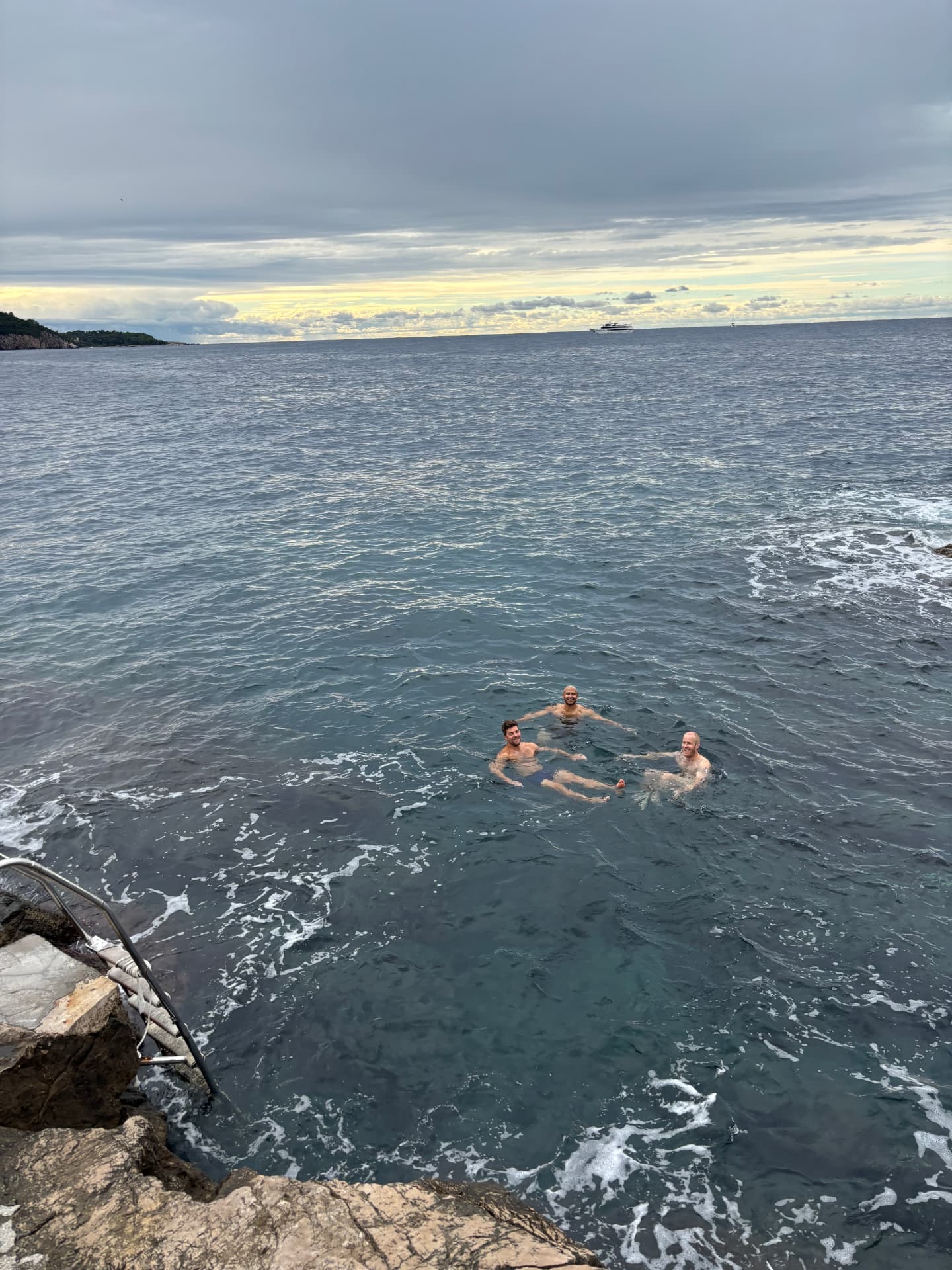 Tre kollegor badar i havet vid klipporna utanför Dubrovnik